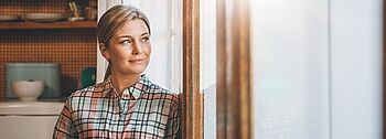Niedertemperaturheizung: Frau mit Tasse schaut aus Fenster