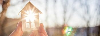 Flachkollektor: Hand hält kleines Holzhaus in die Sonne