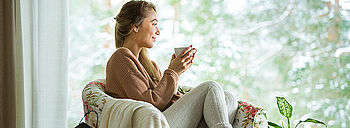 Wärmewende ist wichtiger Teil der Energiewende: Frau trinkt heißen Tee auf gemütlichem Sessel vor Fenster