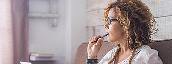 Heizung einbauen Kosten: nachdenkliche Frau sitzt auf Sofa mit Stift im Mund