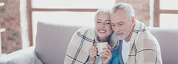 Austauschpflicht nach § 72 GEG: Älteres Pärchen mit Decke auf Couch mit Tasse Tee