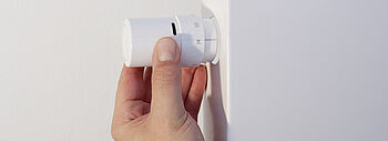 Hochtemperatur Wärmepumpe: Hand dreht Thermostat an einem Heizkörper höher. 