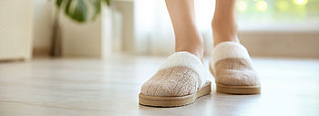 Fußbodenheizung wird nicht warm: Frauenfüße mit warmen Pantoffeln auf Parkettfußboden