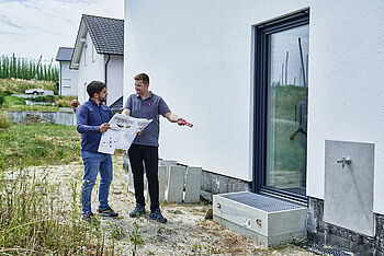 Propan Heizung: Handwerker und Hausbesitzer besprechen Position der Wärmepumpe im Garten.
