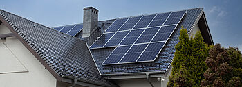 Einspeisevergütung für Photovoltaik: Ihre Vorteile Einspeisevergütung Photovoltaik: Ein Haus samt Dach mit einer Photovoltaik-Anlage, im Hintergrund sind Himmel, Sonne und Vögel zu sehen.