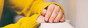 Heizung Druck schwankt: Frau mit Pullover hat Hände auf Heizung