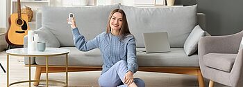 Wärmerückgewinnung: Frau sitzt in warmen Wohnzimmer und bedient ihre Lüftungsanlage
