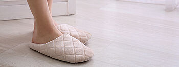 Nachtabsenkung Fußbodenheizung: Füße in Pantoffeln auf Holzfußboden