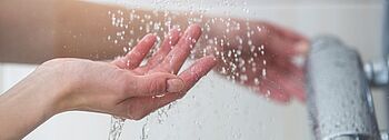 Durchlauferhitzer Kosten: Hände stellen Wassertemperatur ein