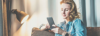 Smarthome Heizung: Frau sitzt mit Smartphone auf Couch