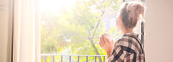 Richtig lüften im Sommer: Praktische Tipps So lüften Sie im Sommer effektiv: Frau sitzt in Sonnenschein vor offenem Fenster