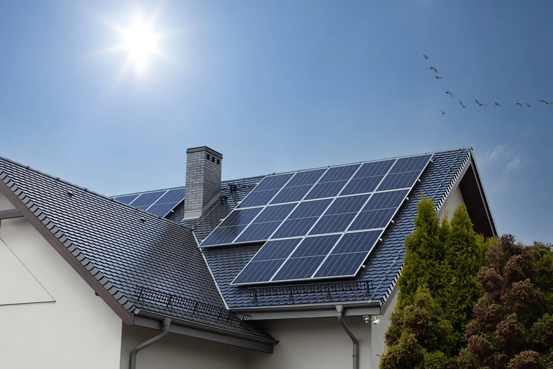 Einspeisevergütung Photovoltaik: Ein Haus samt Dach mit einer Photovoltaik-Anlage, im Hintergrund sind Himmel, Sonne und Vögel zu sehen.