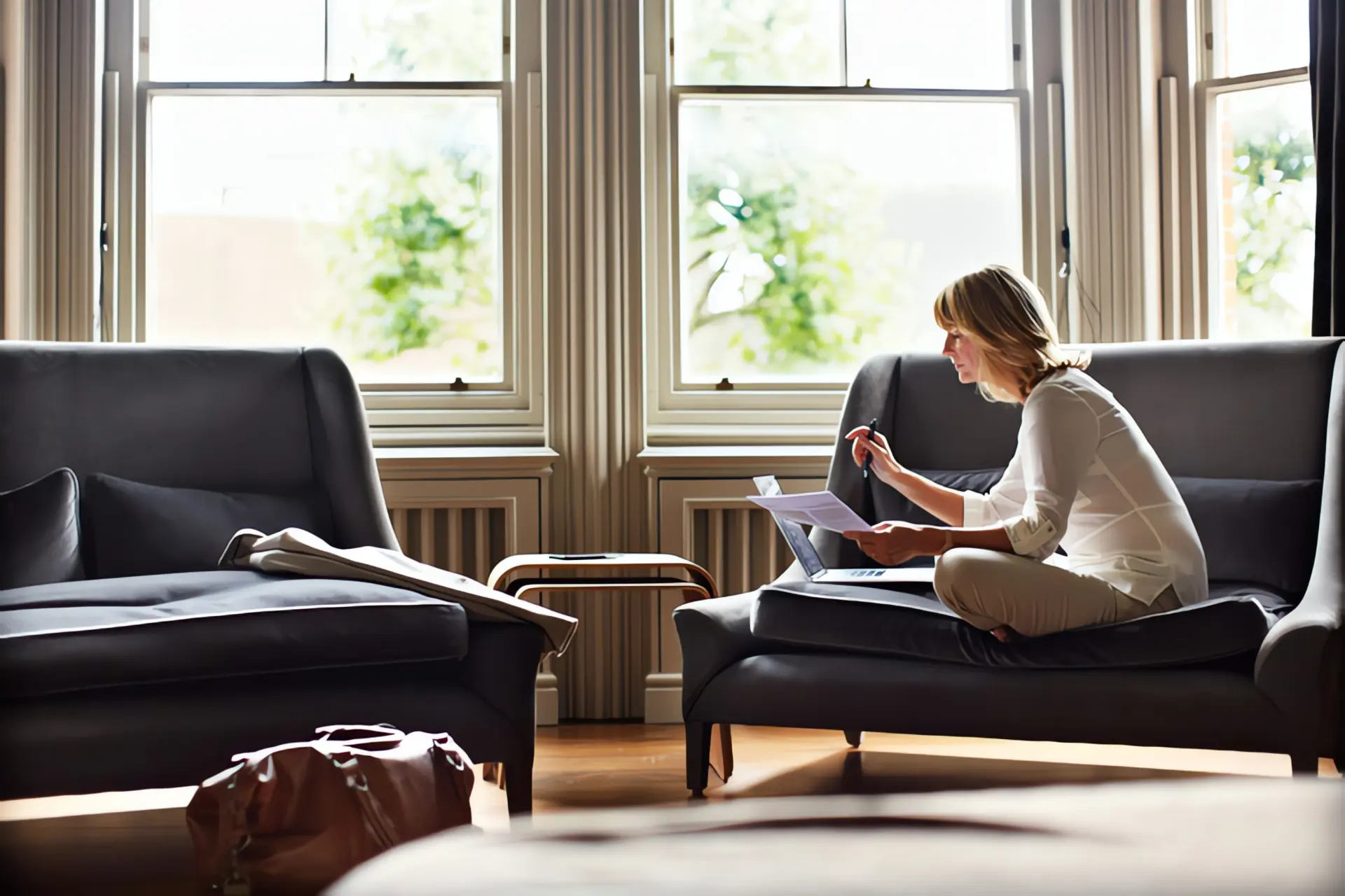 Gastherme mit Warmwasserspeicher: Frau sitzt vor einem Fenster im Wohnzimmer auf einer Couch und studiert Unterlagen.