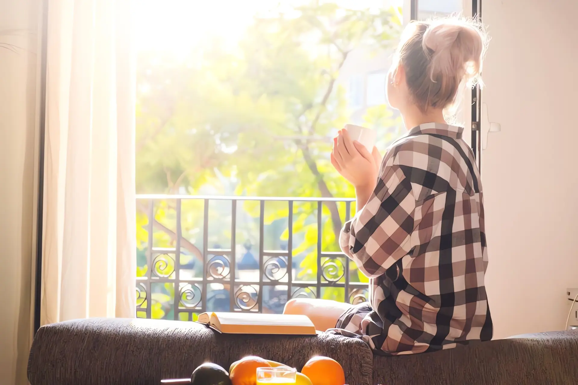 So lüften Sie im Sommer effektiv: Frau sitzt in Sonnenschein vor offenem Fenster