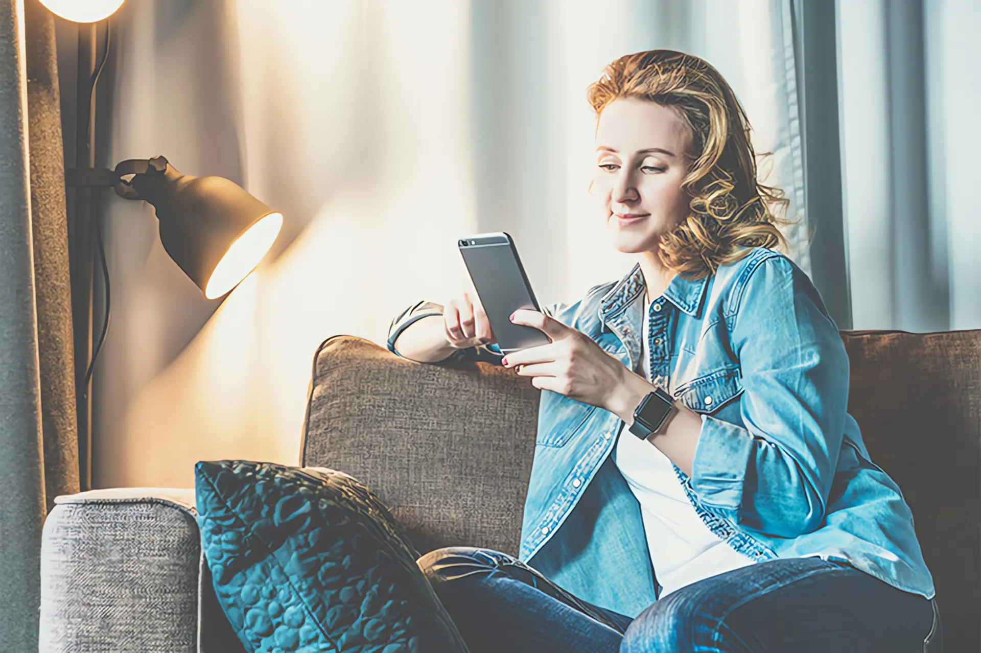 Smarthome Heizung: Frau sitzt mit Smartphone auf Couch
