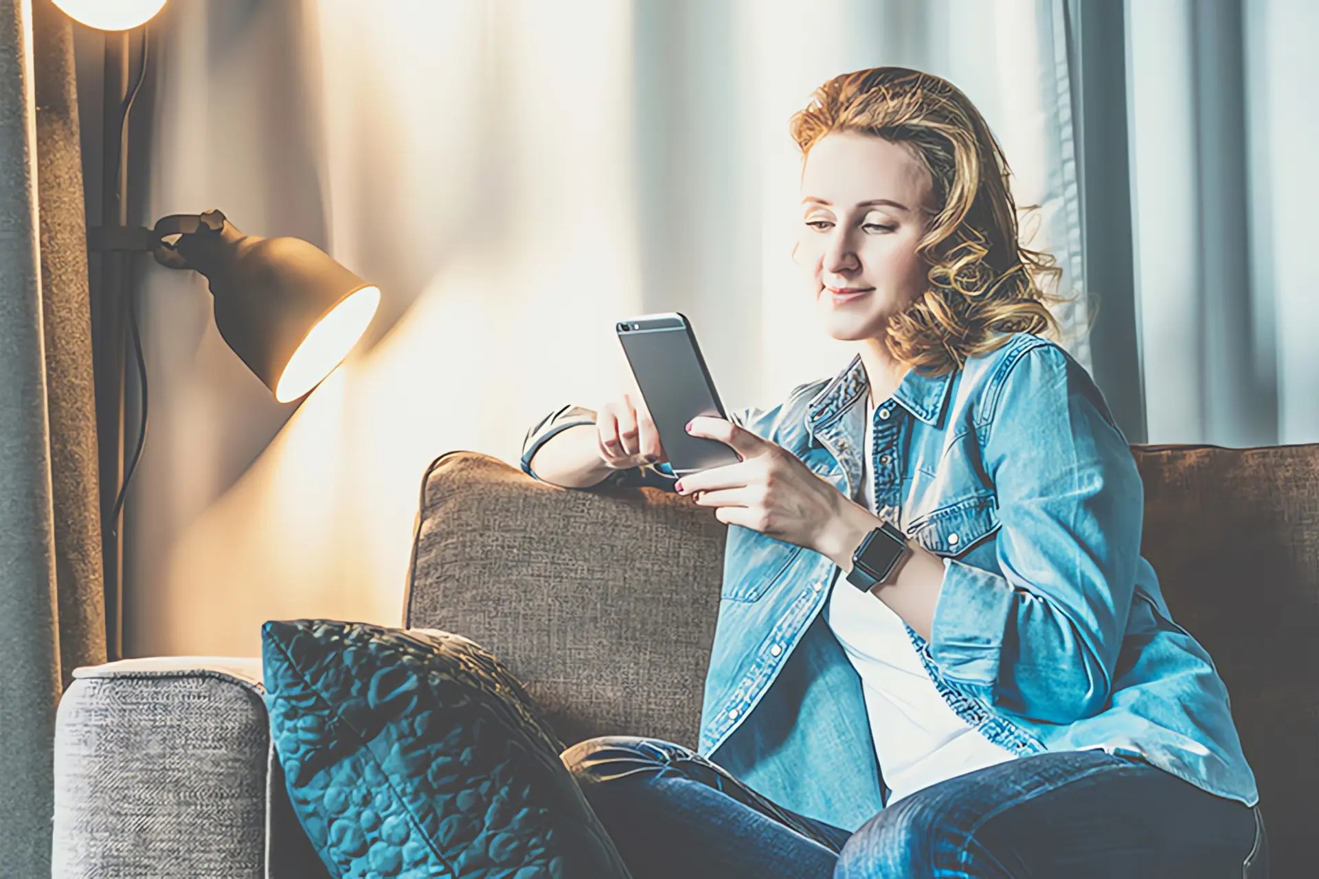 Smarthome Heizung: Frau sitzt mit Smartphone auf Couch