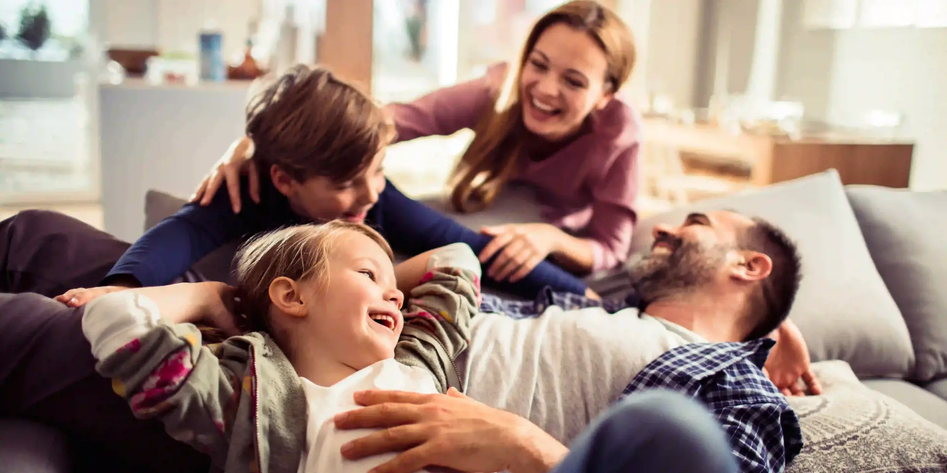 Wärmepumpe austauschen: Das müssen Sie beachten Wärmepumpe austauschen: Familie mit zwei Kindern sitzt lachend auf einer Couch